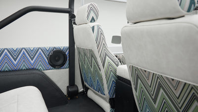 Side view of two front seats inside Classic Ford Bronco with white and patterned upholstery and roll bar