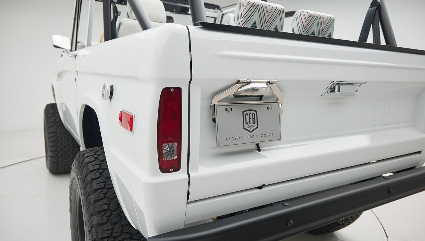 Rear corner of Classic Ford Bronco showing white body, tail light, rear tire, and license plate