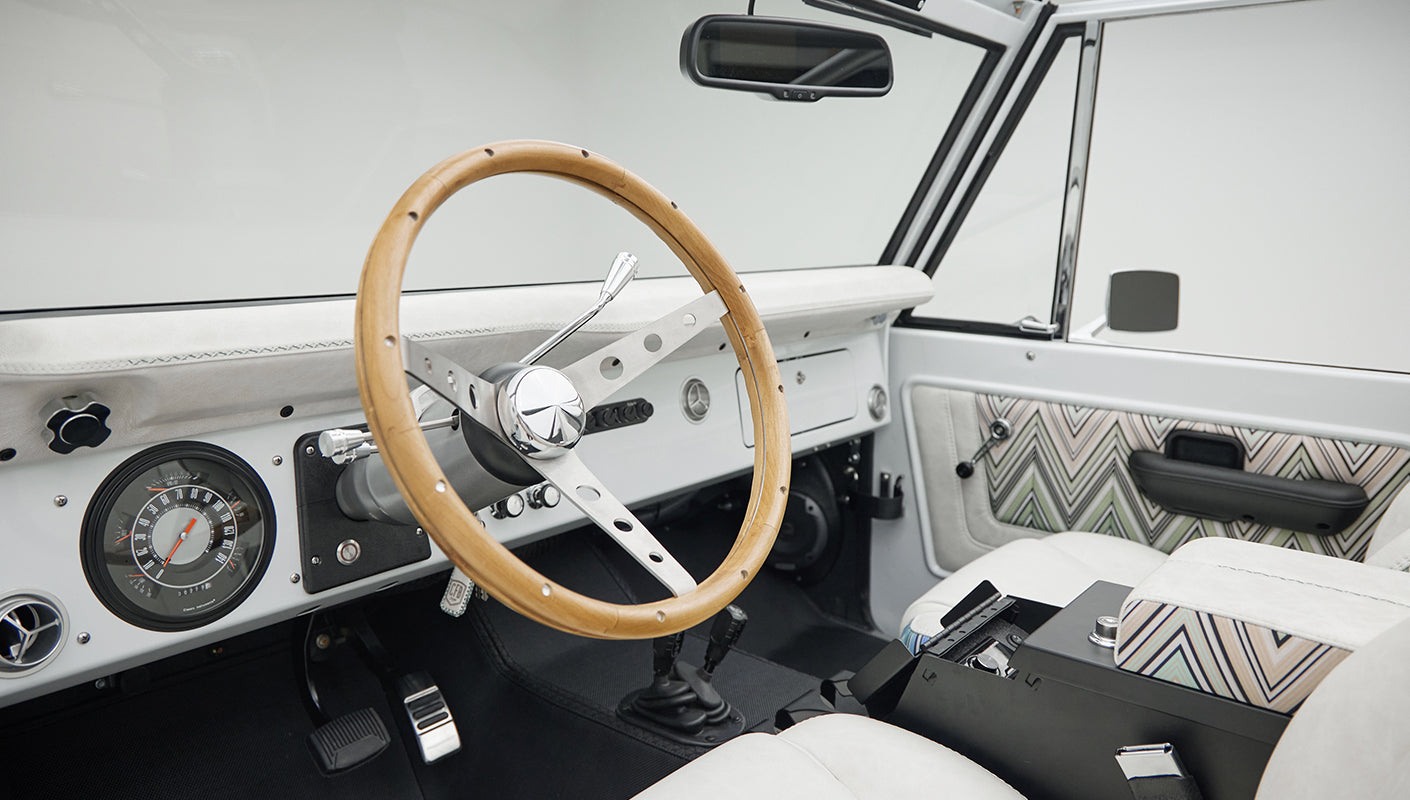 Classic Ford Bronco driver's side interior showing wood steering wheel, dashboard, and white seats