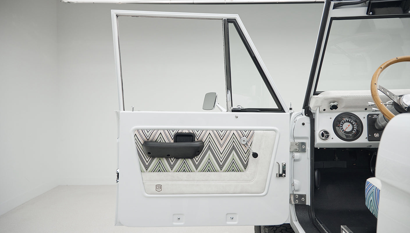 Open driver door of Classic Ford Bronco showing patterned upholstery inside door and white exterior