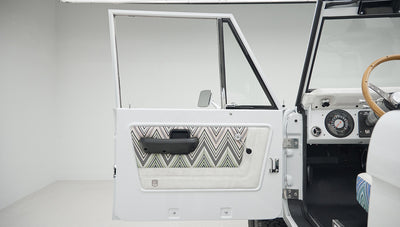 Open driver door of Classic Ford Bronco showing patterned upholstery inside door and white exterior