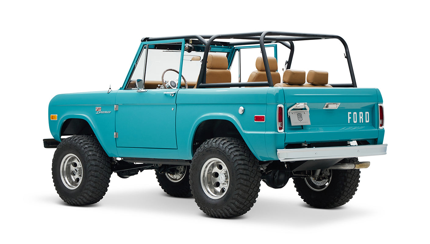 Classic Ford Bronco in Peacock Blue with tan interior, black roll cage, and large off-road tires angled rear view