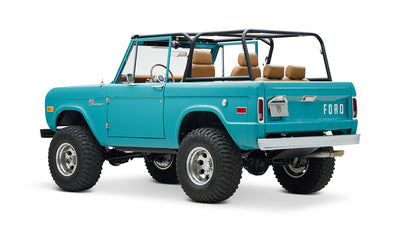 Classic Ford Bronco in Peacock Blue with tan interior, black roll cage, and large off-road tires angled rear view