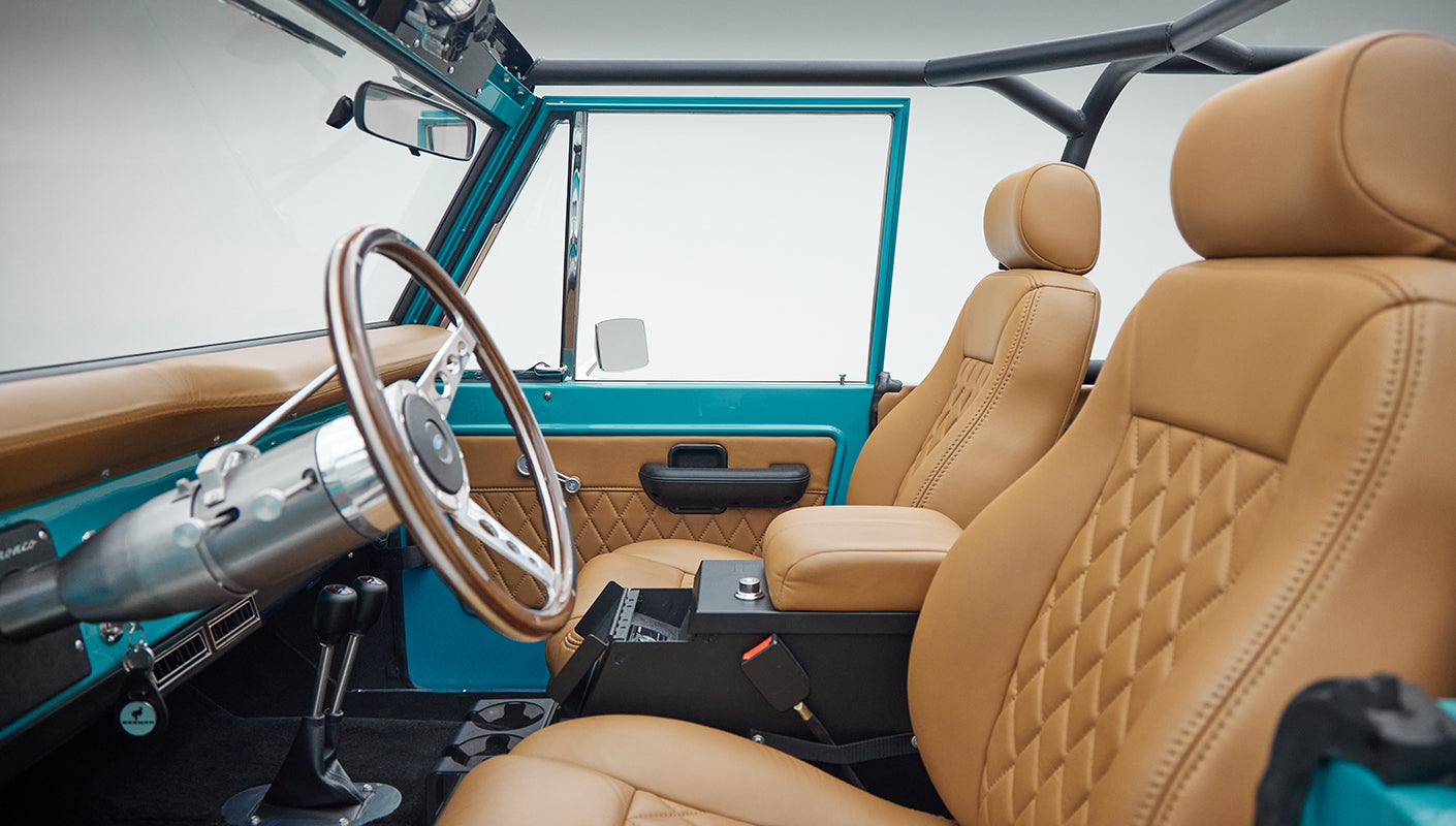 Classic Ford Bronco interior showing tan leather seats and peacock blue door frame