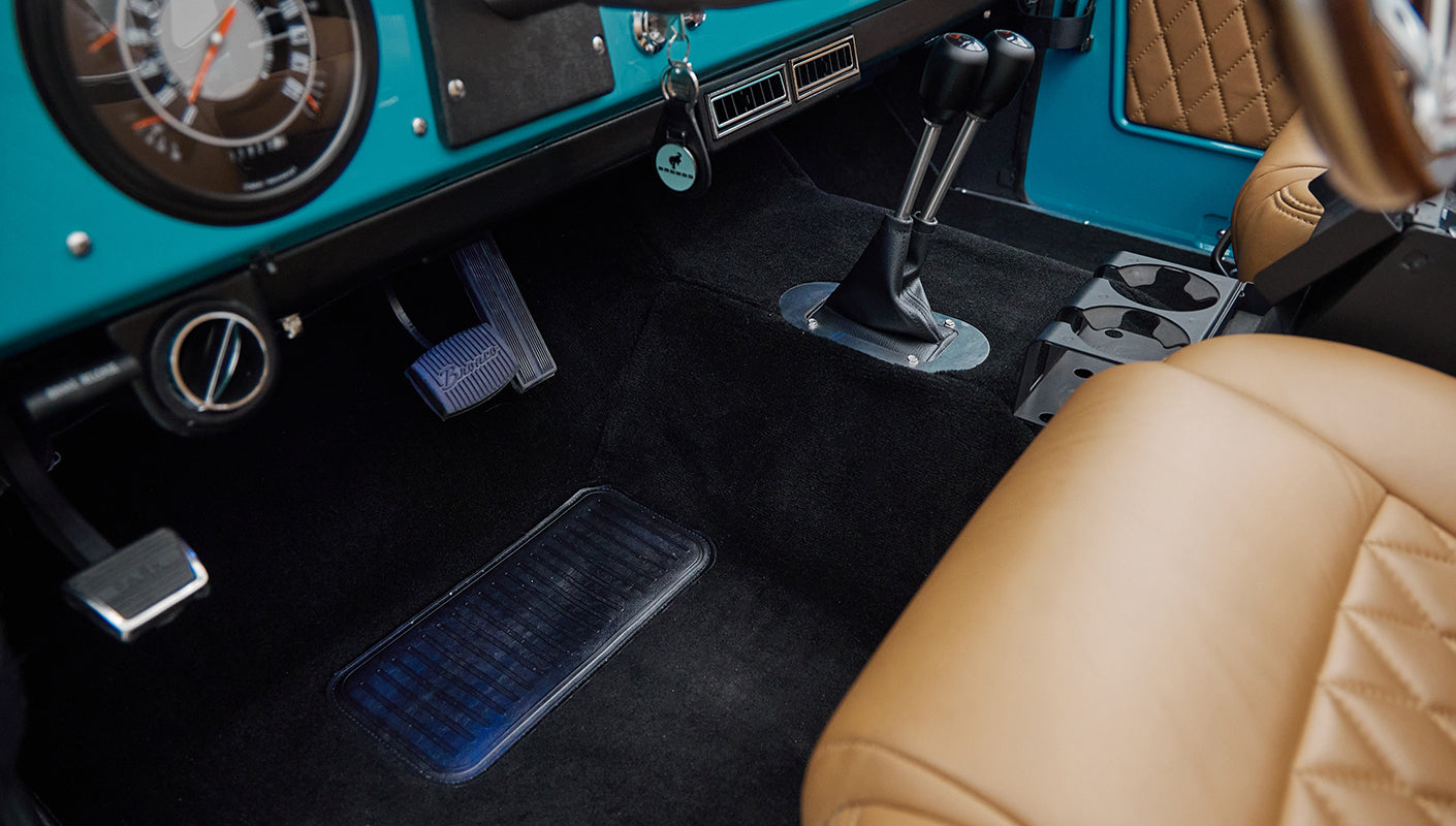 Close-up of steering column and pedals on black carpet inside classic Ford Bronco