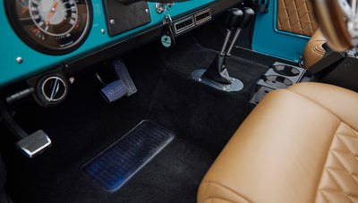 Close-up of steering column and pedals on black carpet inside classic Ford Bronco