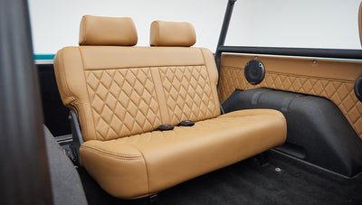 Rear seat view showing tan leather upholstery and black roll cage inside classic Ford Bronco