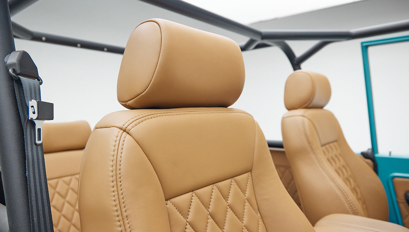 Close-up of tan leather front seats with roll cage and seat belts inside classic Ford Bronco