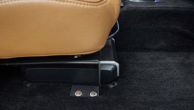 Black subwoofer enclosure mounted on black carpet under tan leather seats inside Classic Ford Bronco