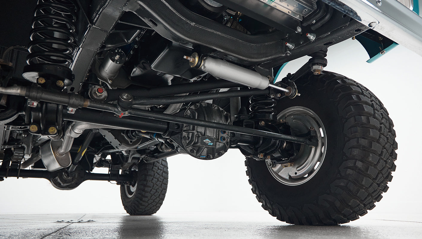 Undercarriage view showing black suspension components, coil springs, and a rugged tire of Classic Ford Bronco