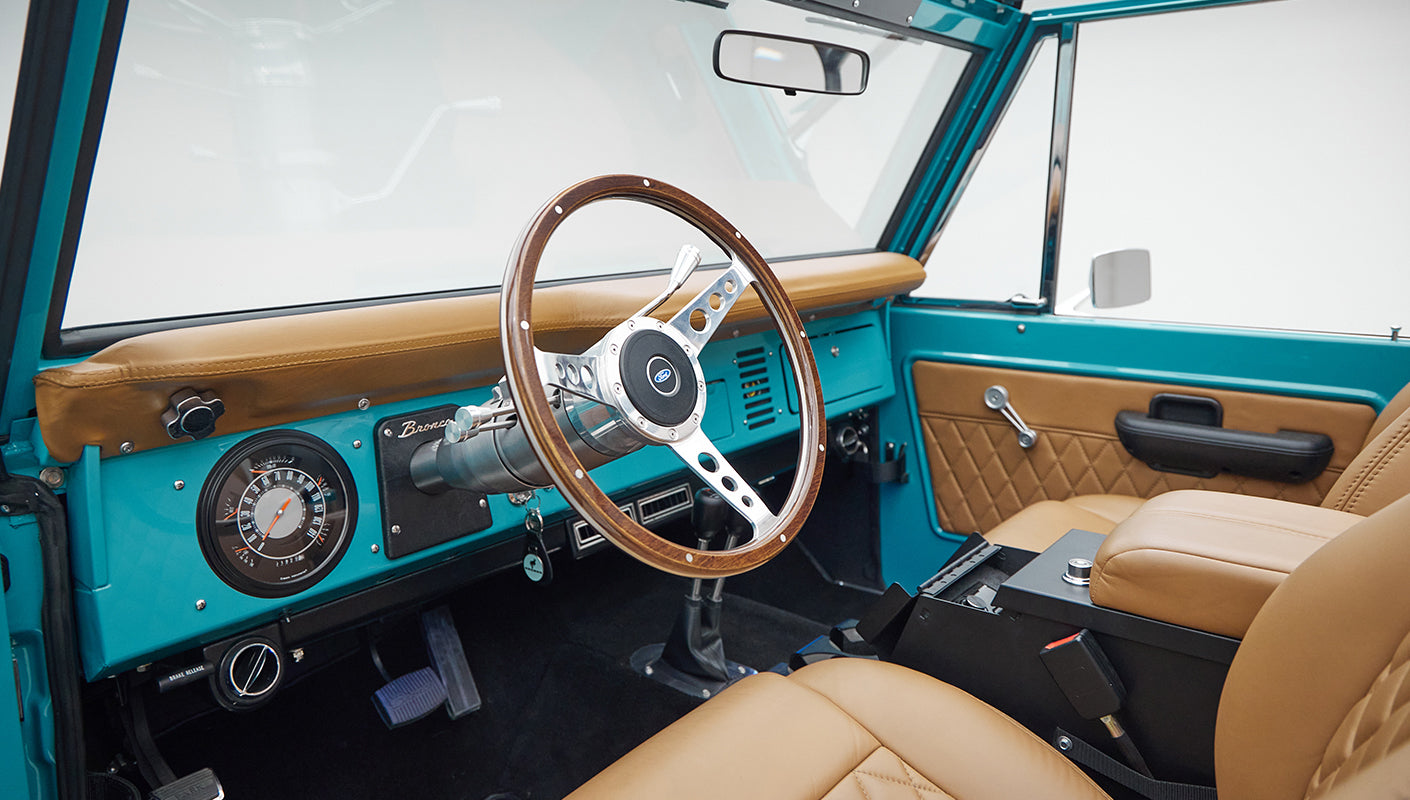 Interior dashboard and wooden steering wheel of Classic Ford Bronco in peacock blue color with tan seats.