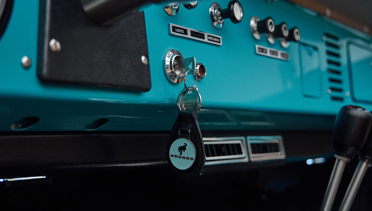 Dashboard with ignition key and Classic Ford Bronco keychain in peacock blue interior.