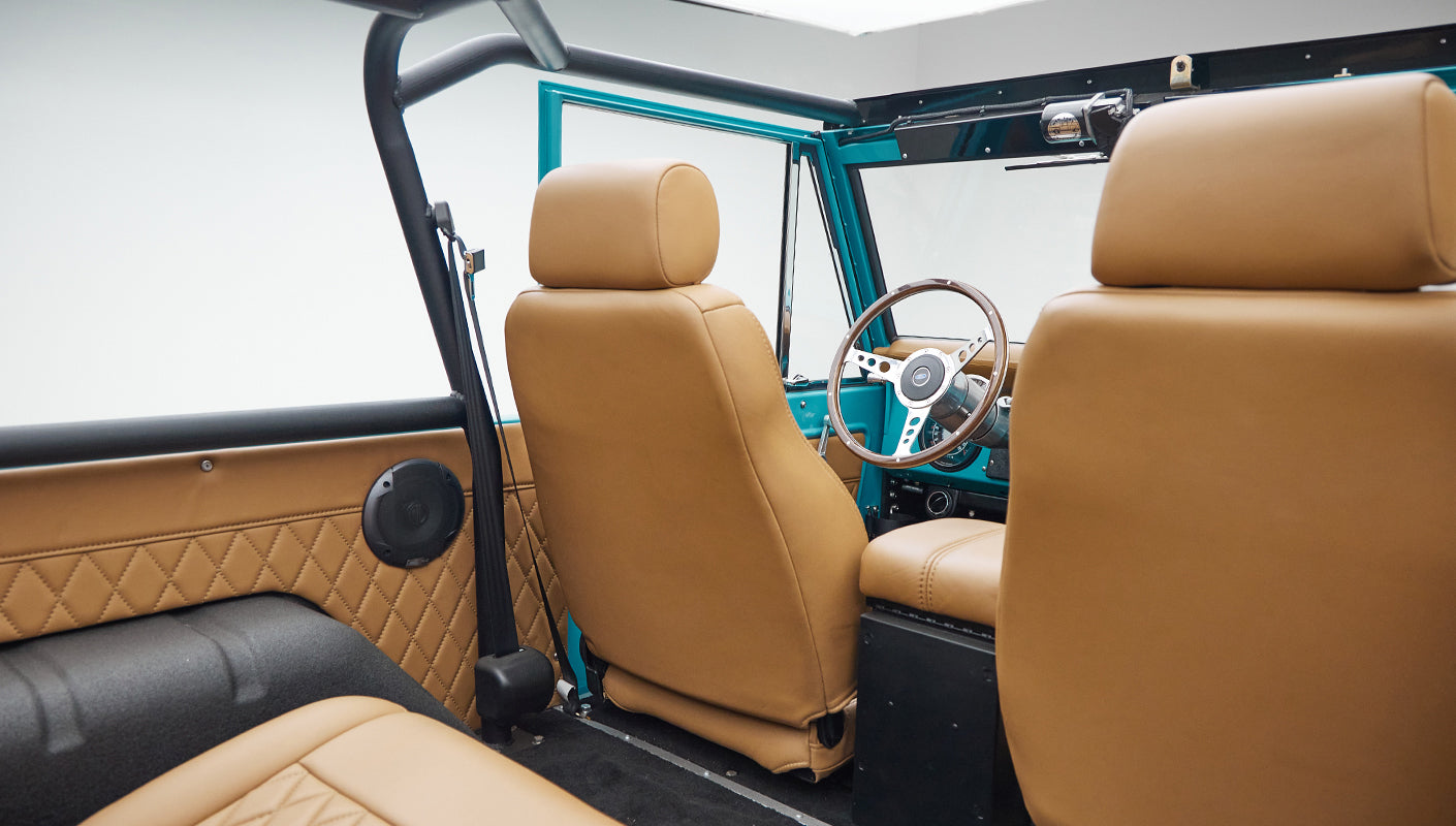 Driver's view of Classic Ford Bronco interior showing dashboard, steering wheel, and tan seats.