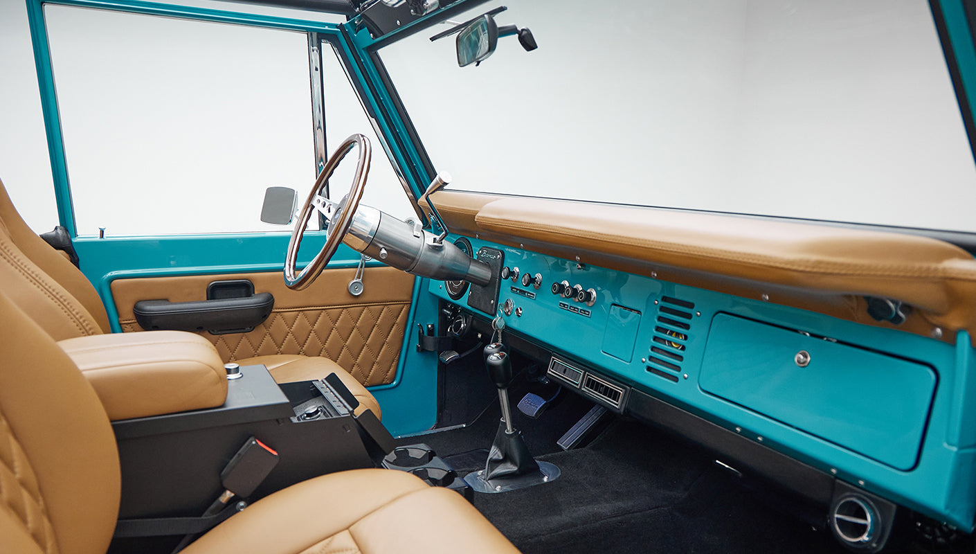 Side view of interior cabin of Classic Ford Bronco with peacock blue doors and tan leather seats.