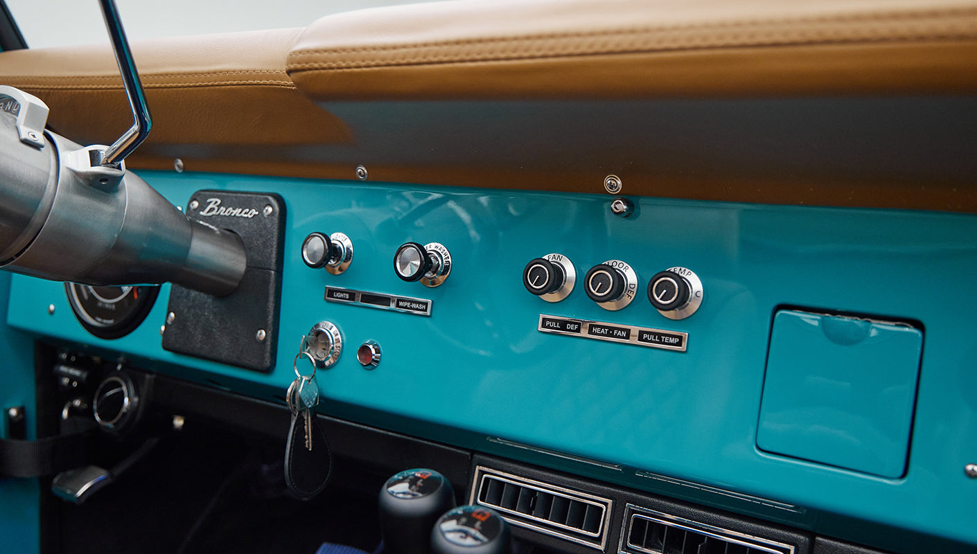 Back seats and roll cage inside Classic Ford Bronco with tan leather and peacock blue interior.