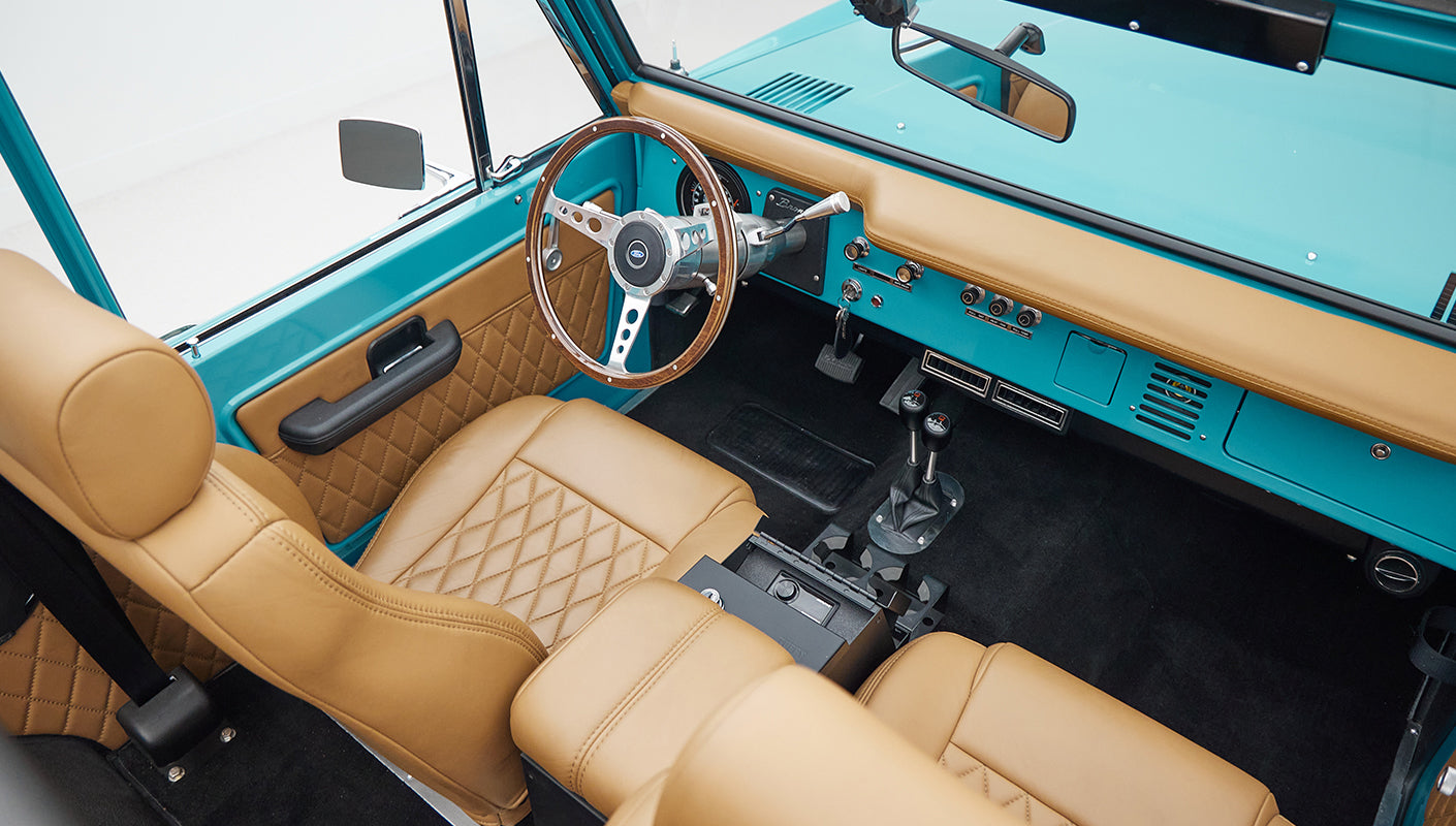 Side view of driver's seat and interior roll cage of Classic Ford Bronco with tan leather seats.