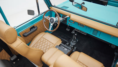 Side view of driver's seat and interior roll cage of Classic Ford Bronco with tan leather seats.