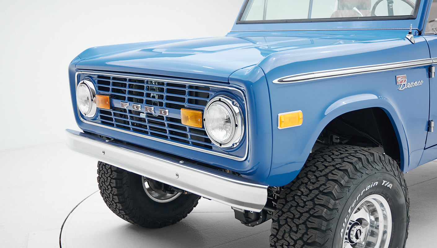 Front corner close-up of Classic Ford Bronco with chrome grille, round headlights, and off-road tires