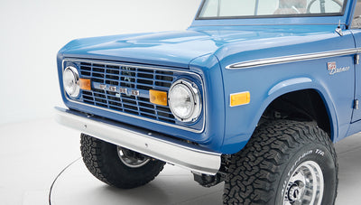 Front corner close-up of Classic Ford Bronco with chrome grille, round headlights, and off-road tires