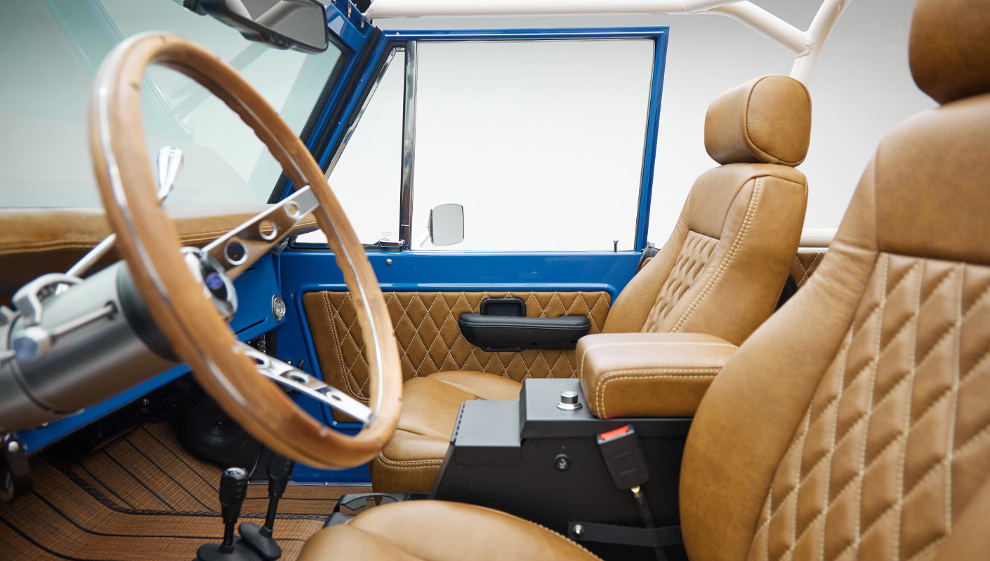 Close-up side view of steering wheel and driver seat in Classic Ford Bronco interior with tan upholstery