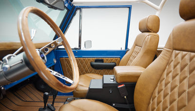 Close-up side view of steering wheel and driver seat in Classic Ford Bronco interior with tan upholstery