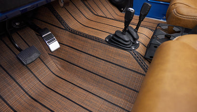 Brake and accelerator pedals with brown textured floor mat and two gear shift levers in Classic Ford Bronco