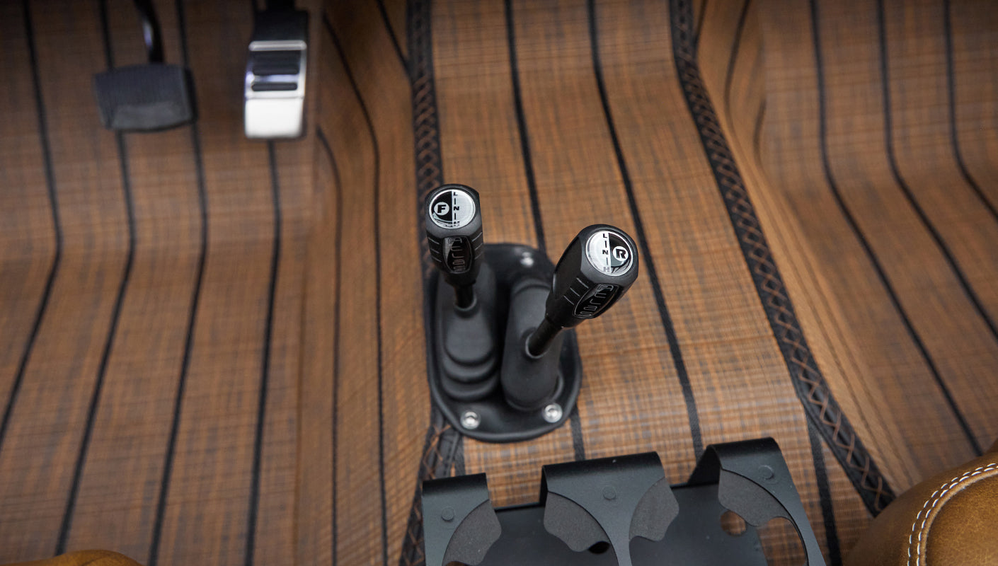 Two gear shift levers on brown striped floor mat with tan leather seat edges in Classic Ford Bronco interior