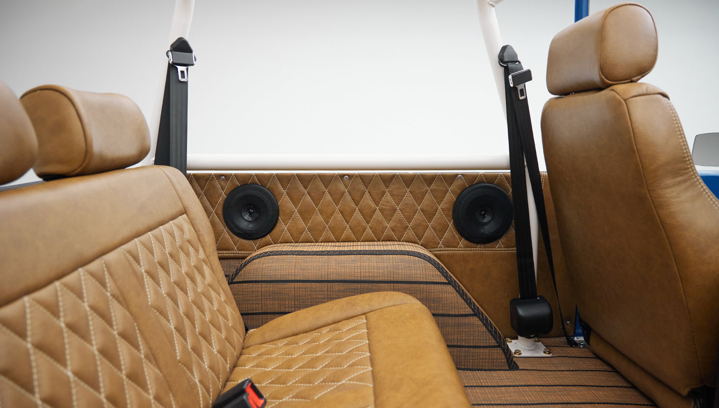 Rear passenger seat area of Classic Ford Bronco with tan diamond-stitched upholstery and black seat belts