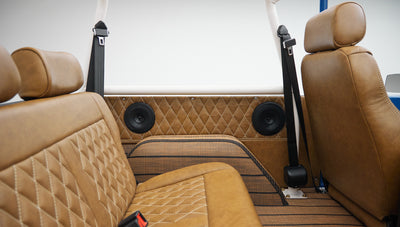 Rear passenger seat area of Classic Ford Bronco with tan diamond-stitched upholstery and black seat belts