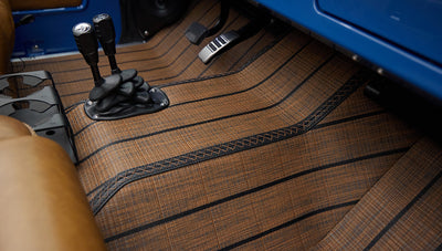 Brown textured floor mat extending through footwell with pedals and plastic brackets visible in Classic Ford Bronco