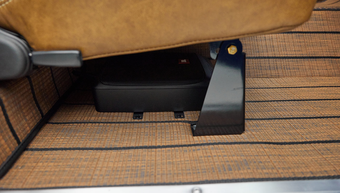 Black subwoofer or speaker box mounted under tan textured floor mat in Classic Ford Bronco footwell