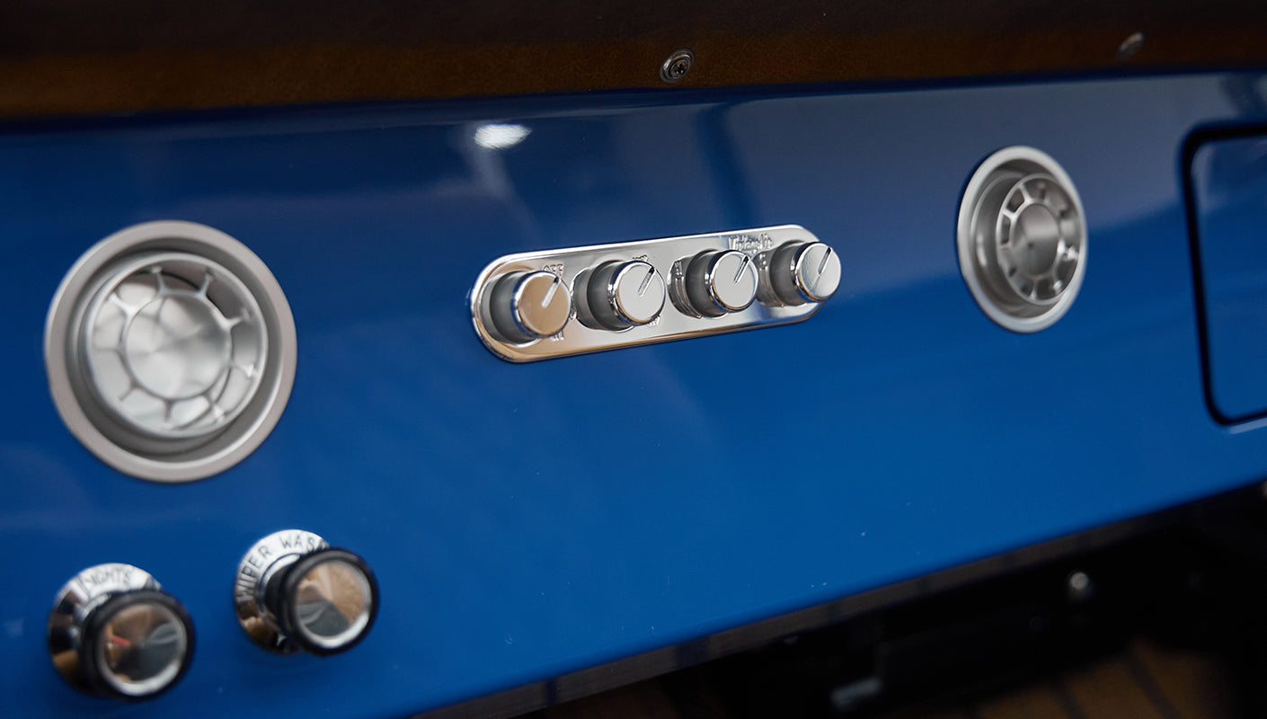 Dashboard controls with chrome knobs and air vents on blue panel of Classic Ford Bronco