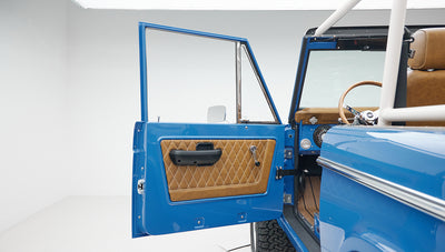 Open driver side door showing blue interior panel with diamond stitching on tan leather in Classic Ford Bronco