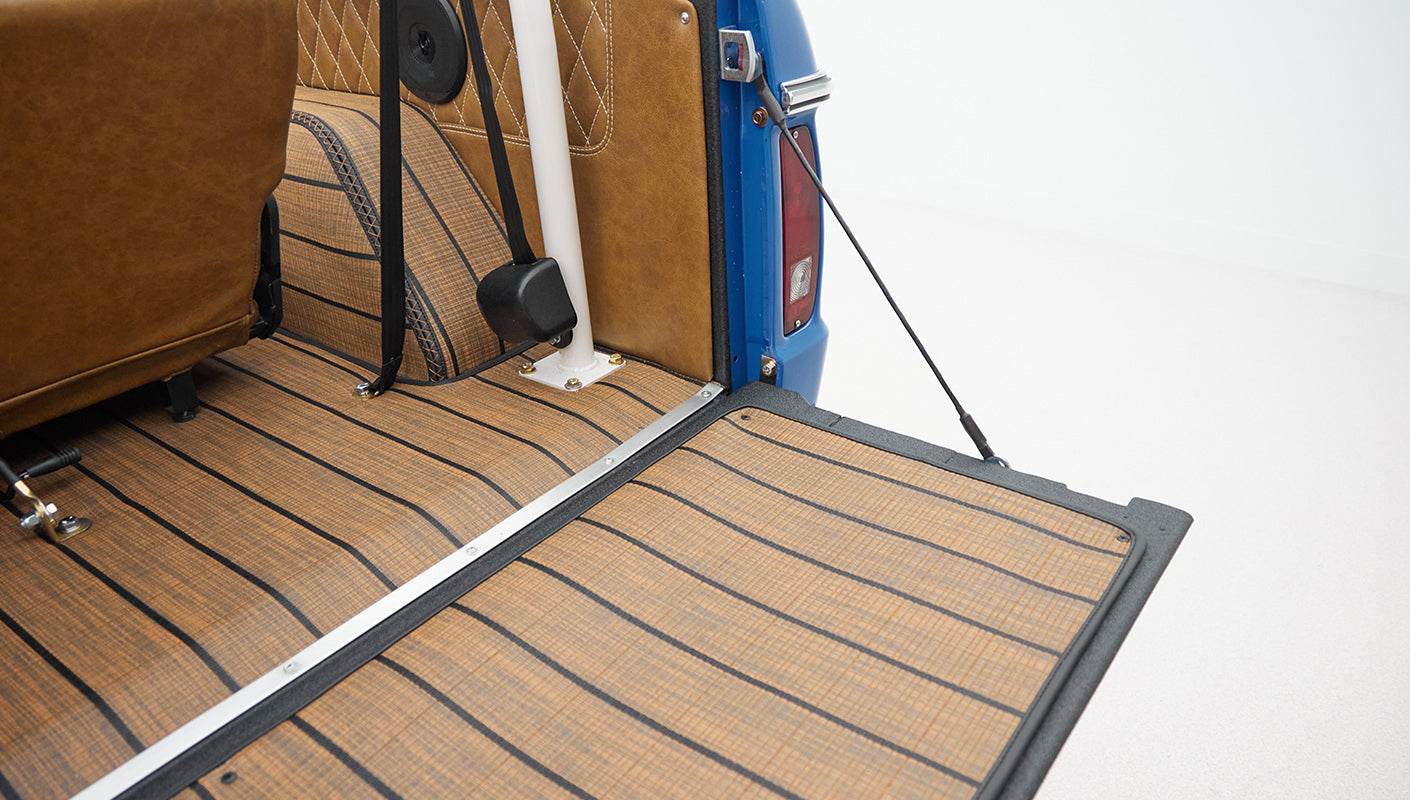 Open rear cargo area of Classic Ford Bronco showing seat backs, tan diamond-stitched upholstery, and wood-effect flooring