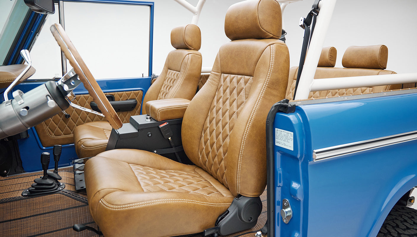 Interior front seats of Classic Ford Bronco in tan leather with diamond stitching and blue door frame