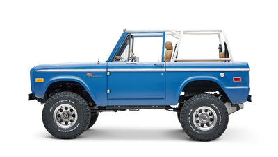 Side profile of blue Classic Ford Bronco with large off-road tires on white background