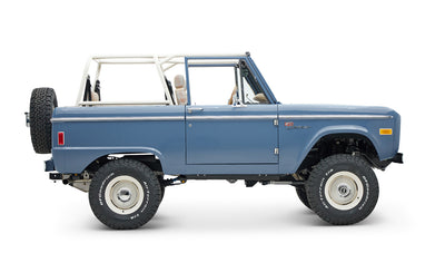 Classic Ford Bronco in light blue, side profile with off-road tires and white roll cage without roof.