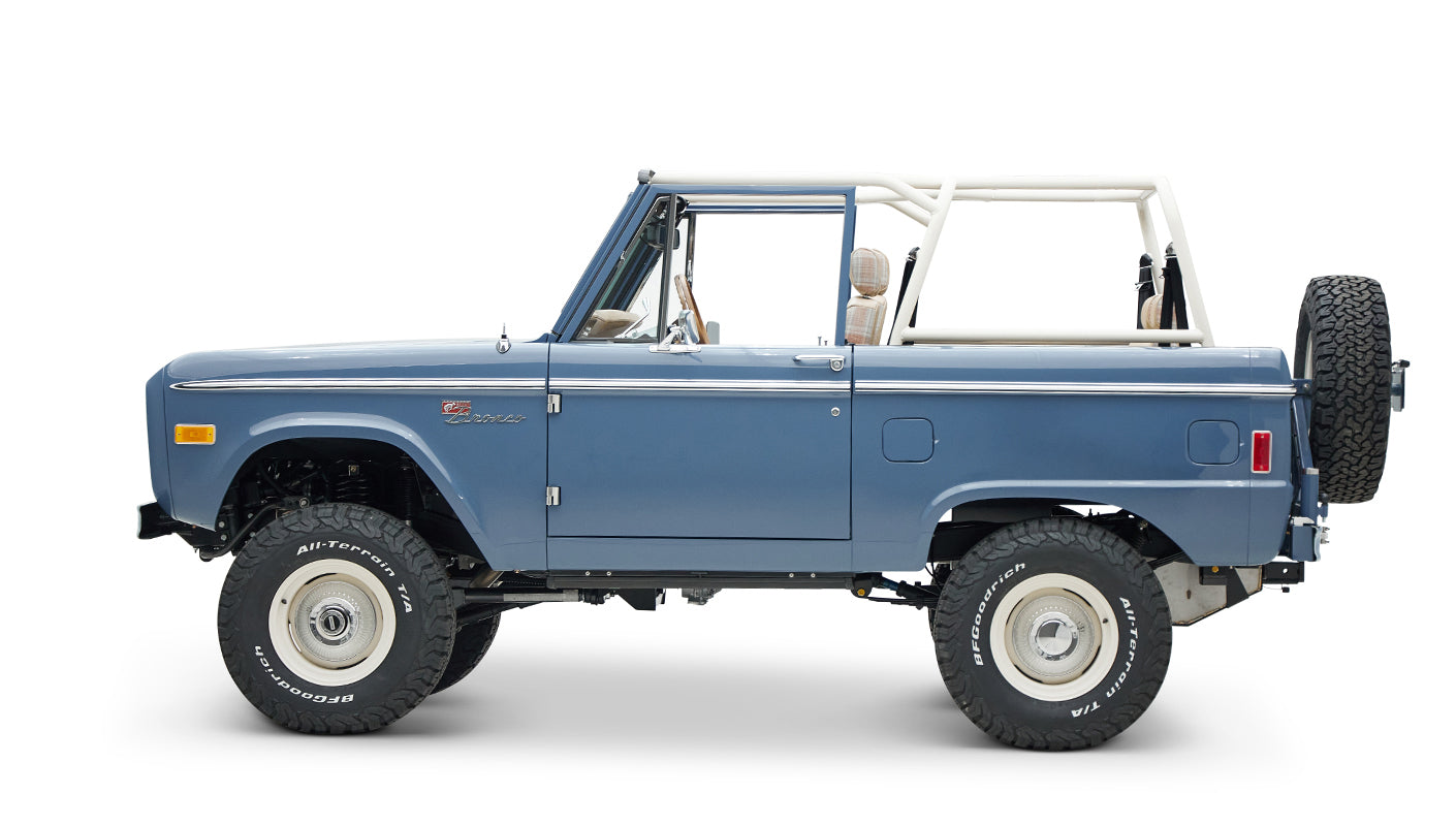 Classic Ford Bronco in light blue, side profile with lifted suspension and white wheels without roof.