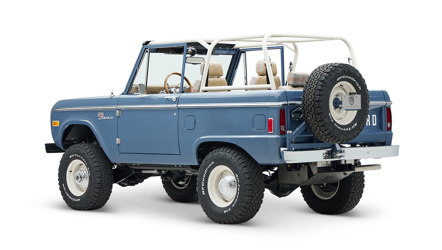 Classic Ford Bronco in light blue, rear side angle showing spare tire mounted on back with white roll cage.