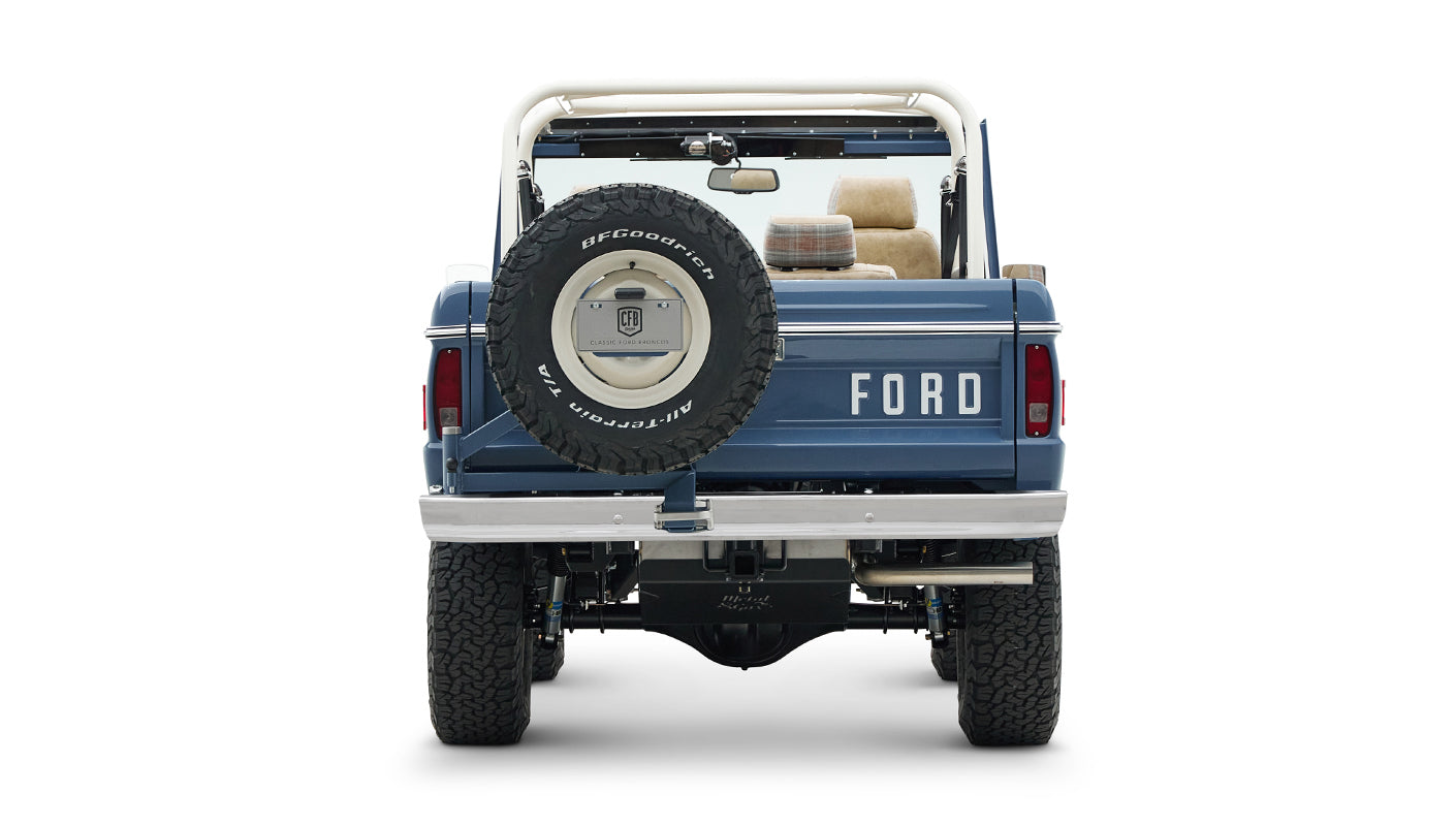 Rear view of Classic Ford Bronco in blue with mounted spare tire and white roll cage