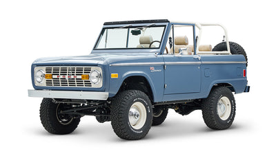 Classic Ford Bronco in light blue, front side angle with lifted suspension and white wheels.