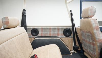 Interior view of rear seats and side door panels in tan and plaid fabric with black seat belts and speakers