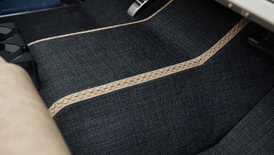 Dark grey floor mat with beige stitched trim inside vehicle
