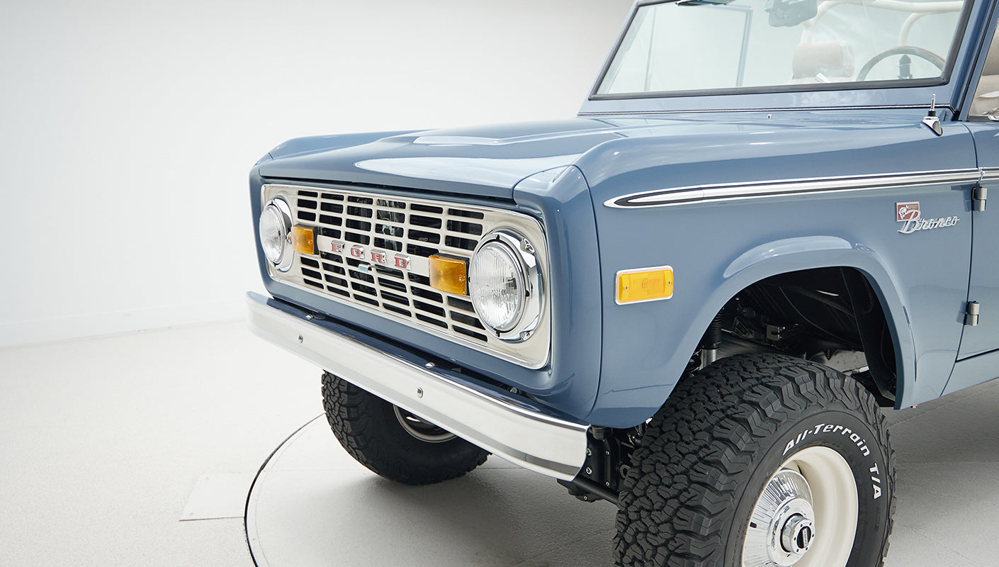 Front side view of Classic Ford Bronco in blue showing grille, headlights, and tire tread