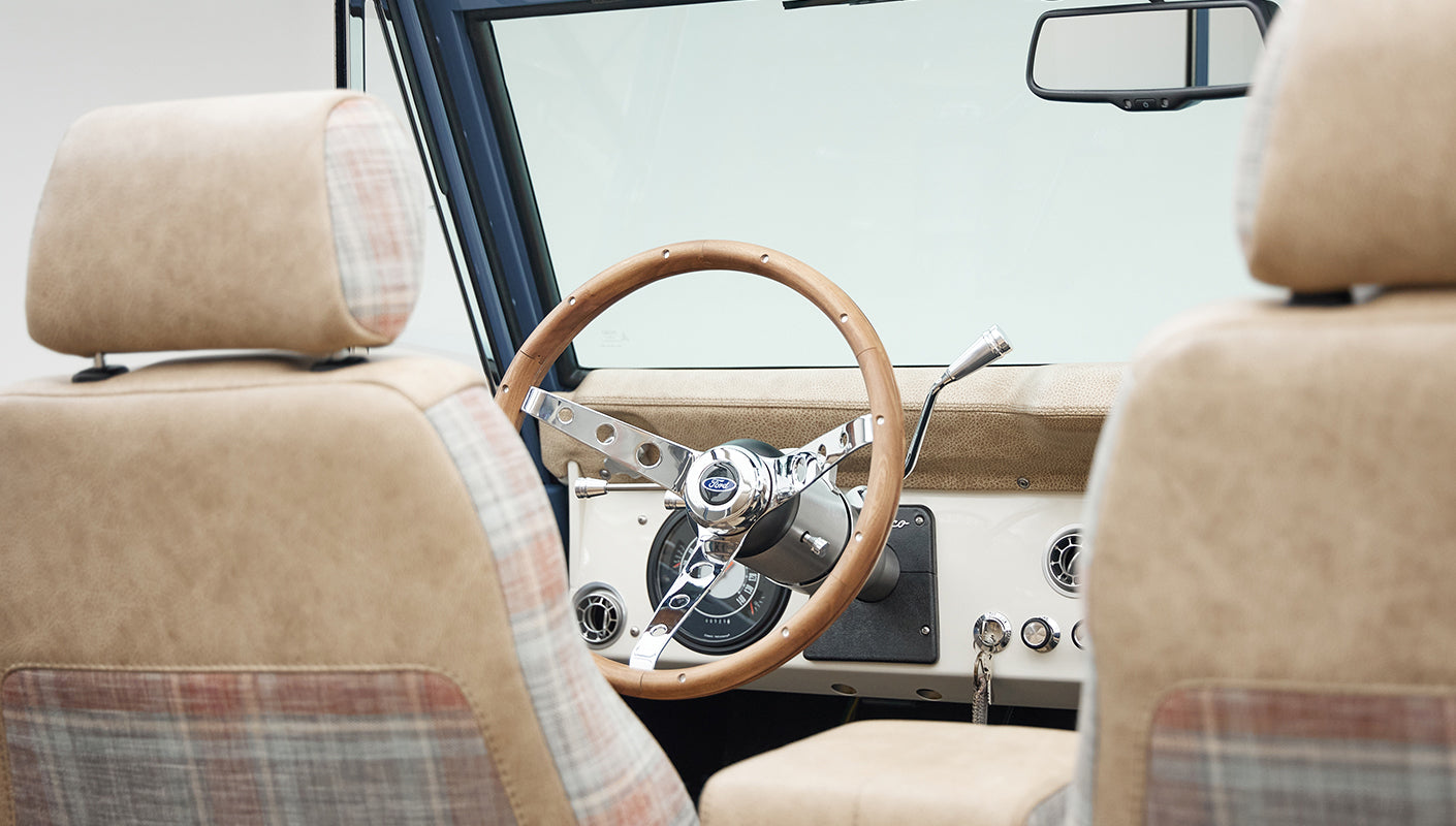 Classic Ford Bronco interior showing a wood-trimmed steering wheel and beige plaid seats