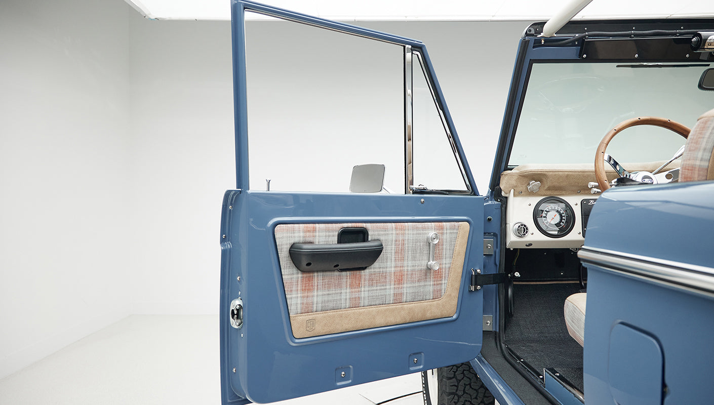 Open blue door of Classic Ford Bronco showing plaid fabric interior panel and black handle