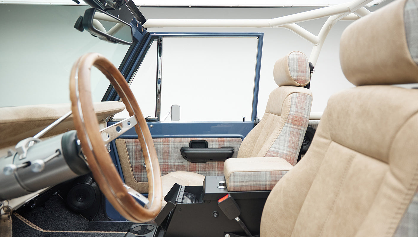 Interior side view of Classic Ford Bronco with plaid and beige seats, wooden steering wheel