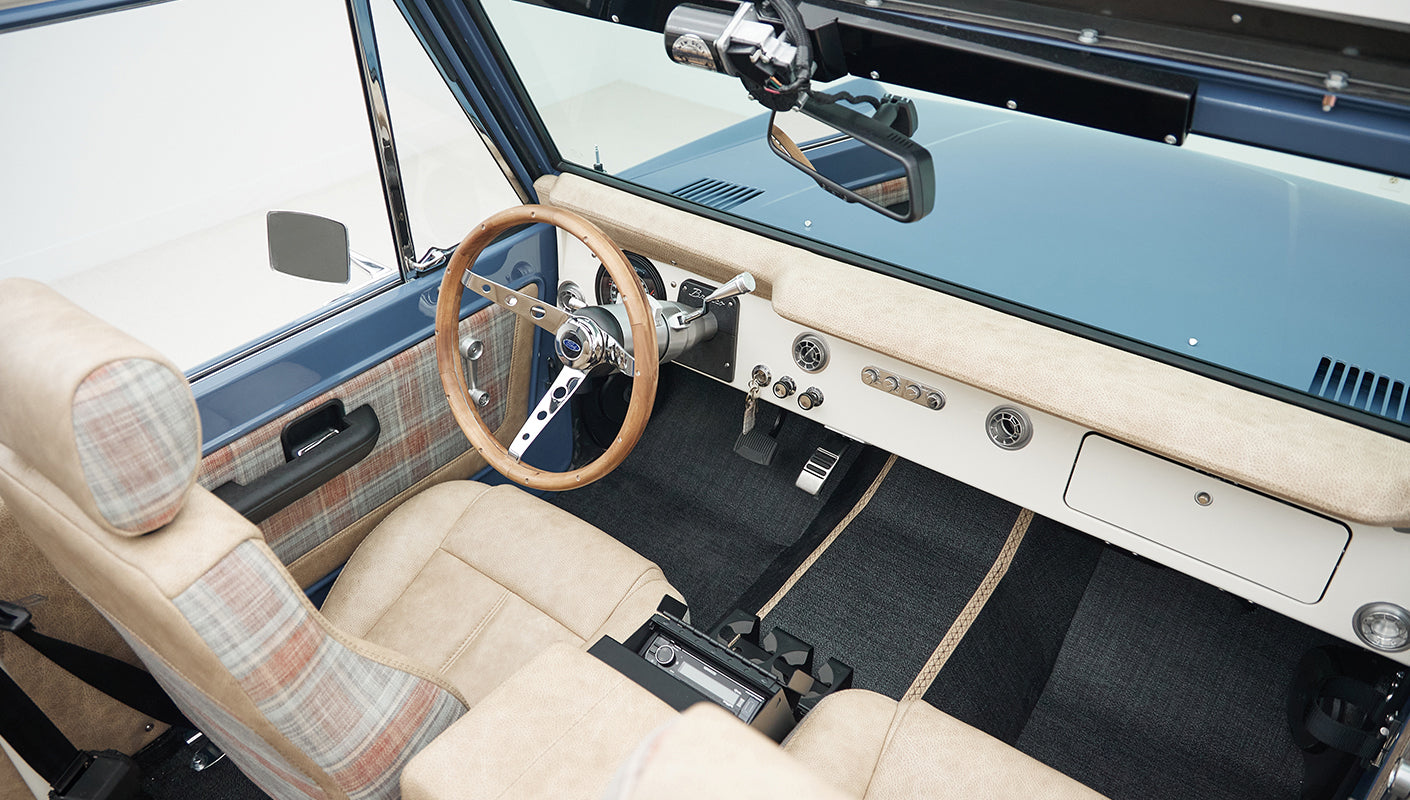 Wide view of Classic Ford Bronco interior showing wood steering wheel, dashboard, and beige seats