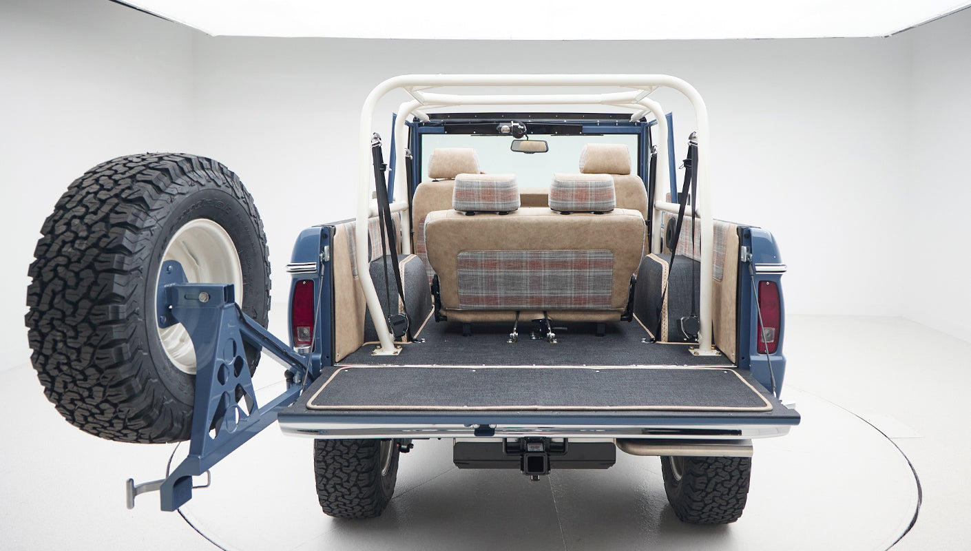Rear view of Classic Ford Bronco showing tailgate open and beige plaid seats inside
