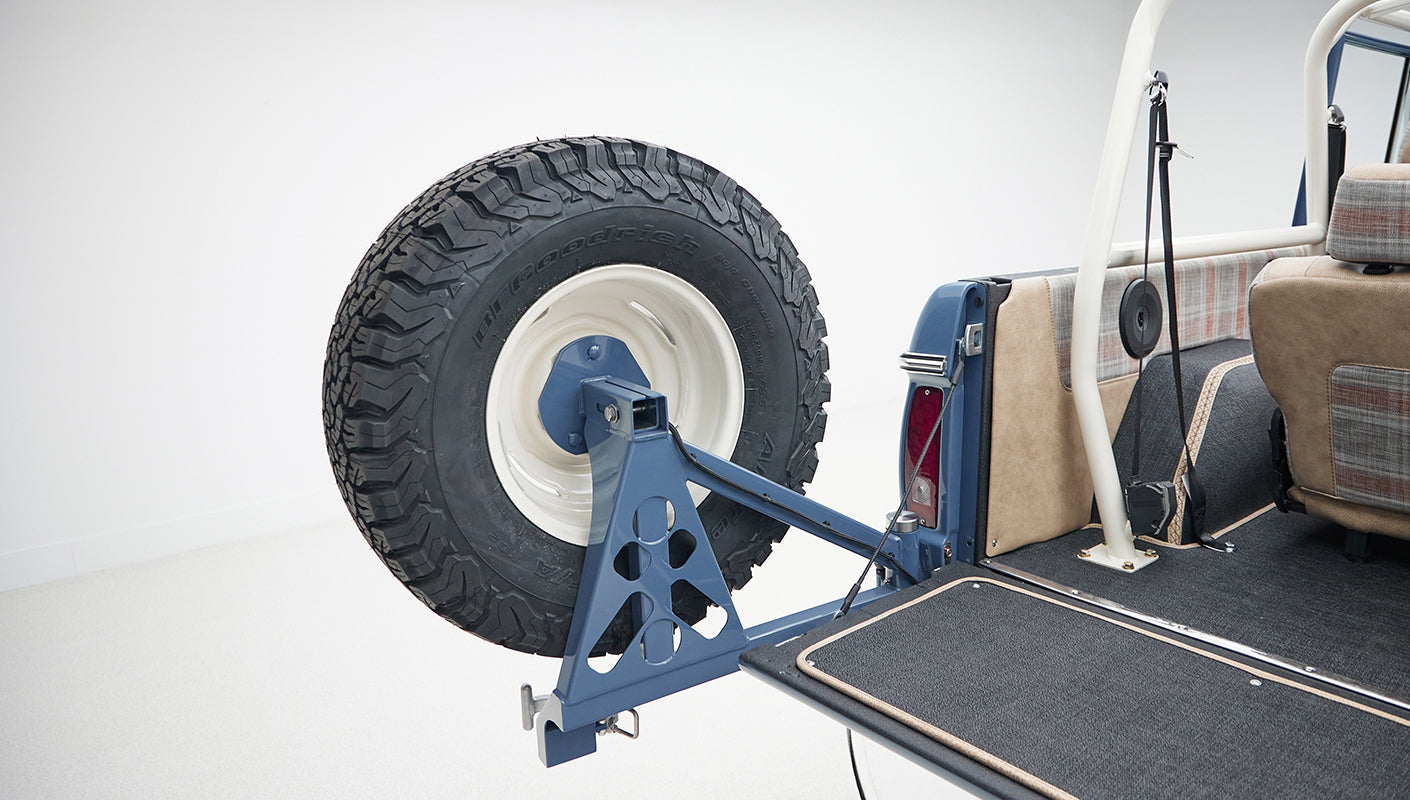Spare tire mounted on the back of Classic Ford Bronco with blue body and beige interior